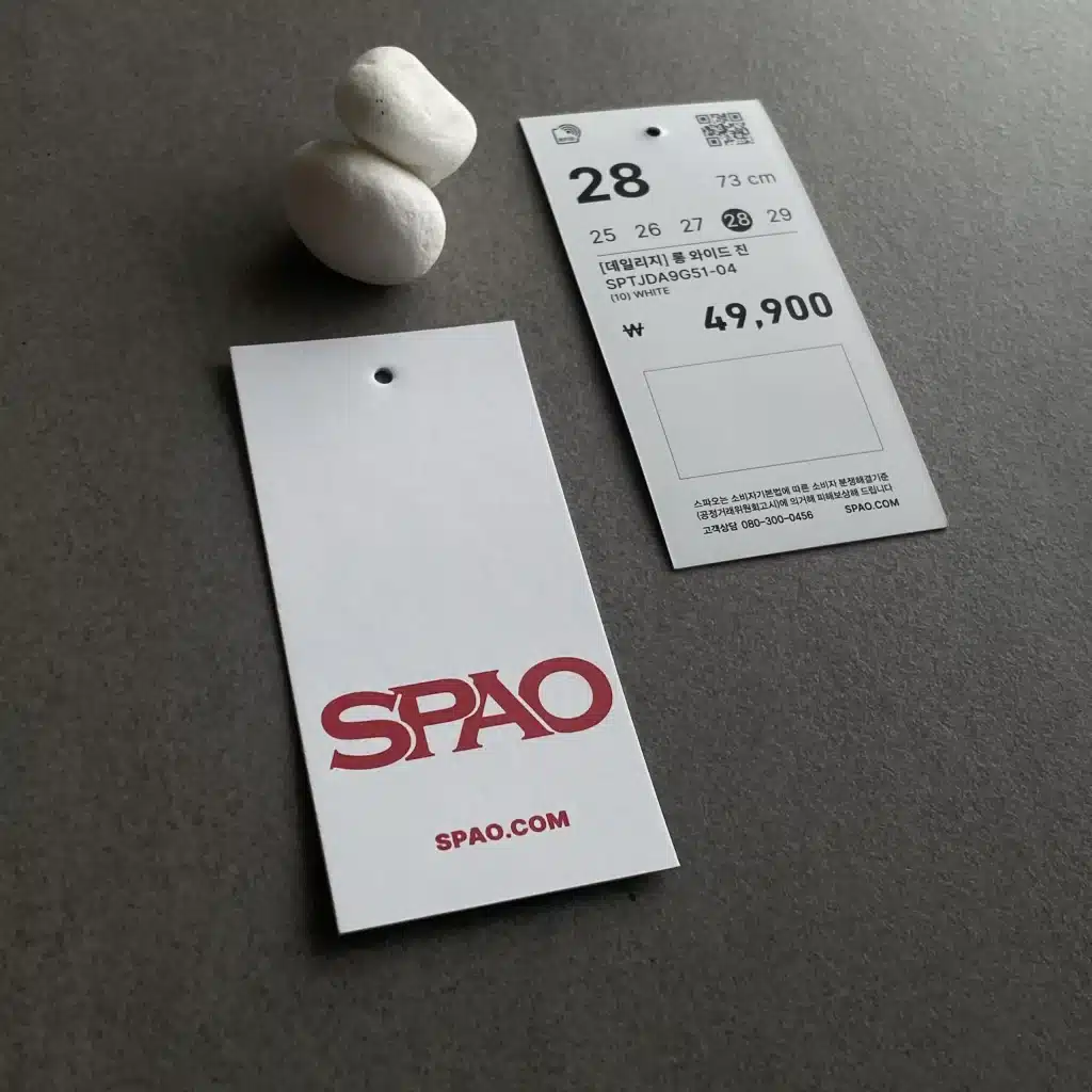 Hangtags quần áo SPAO với thiết kế tối giản, logo đỏ trên nền trắng và thông tin sản phẩm rõ ràng.
